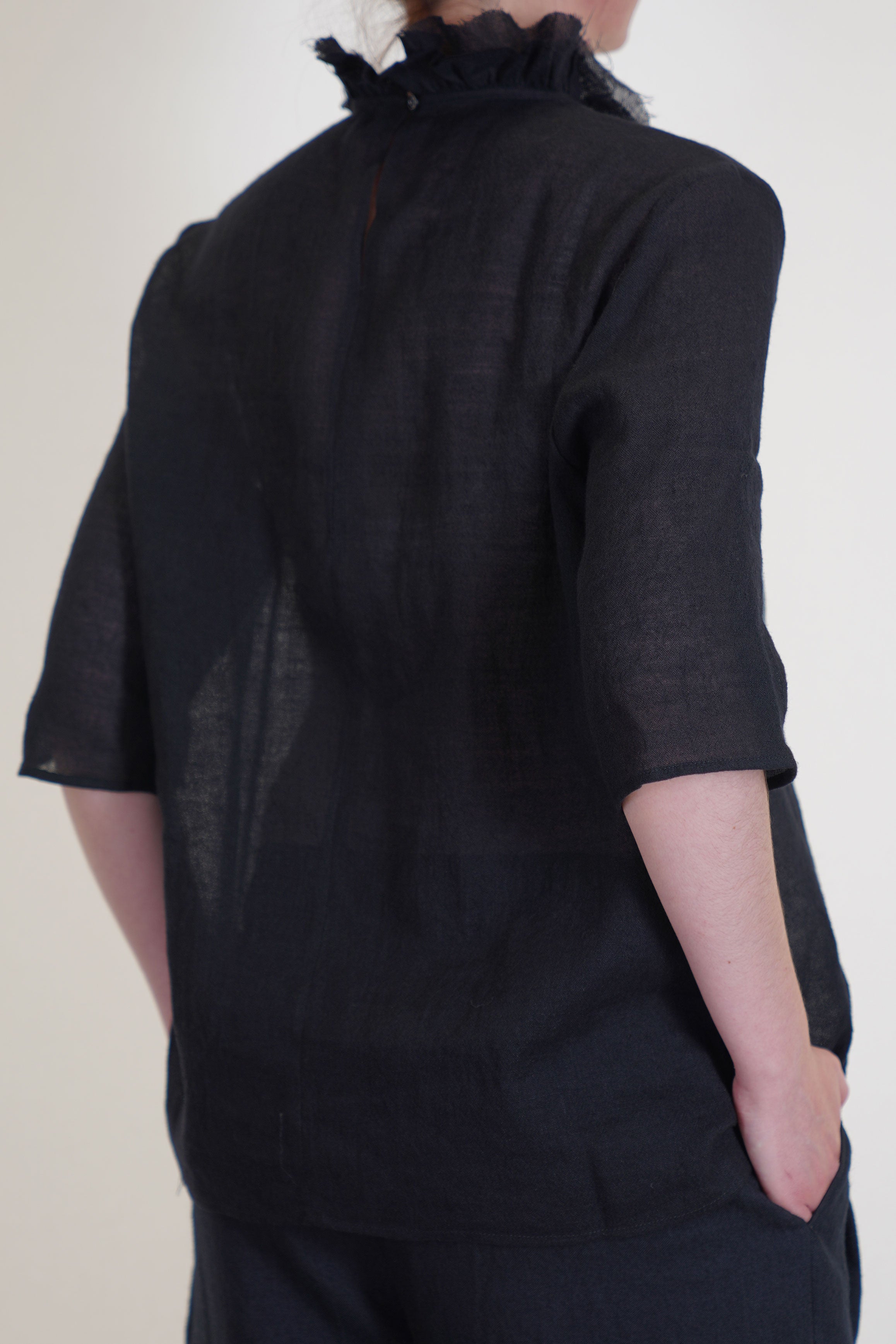 back view of apuntob (a.b) shirt black single button opening at the back, high collar with ruffle details