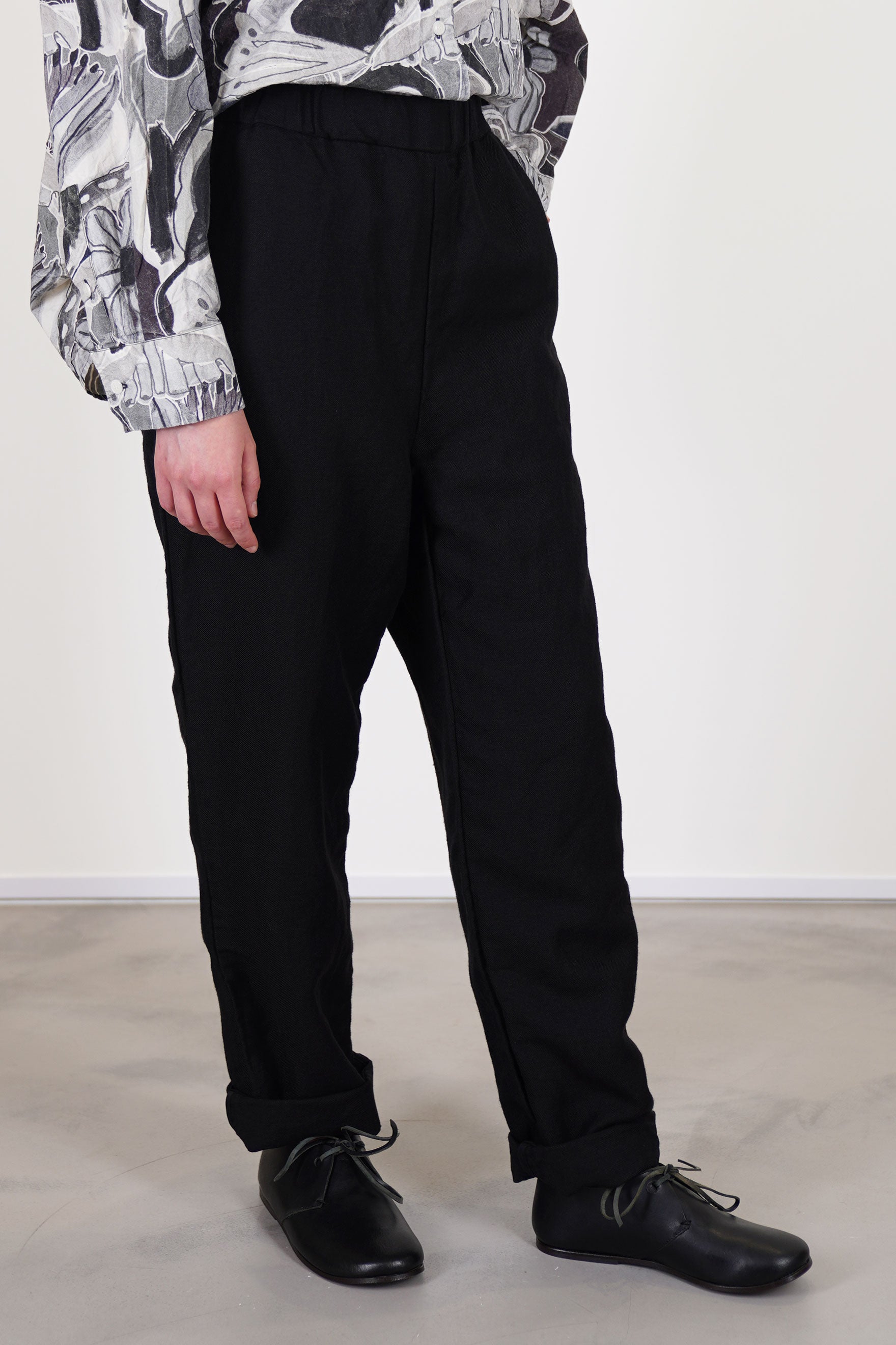 side view of casey casey long chasse pants black slim elasticated waistband with a hidden adjustable drawstring, long striaght legs and side pocket details