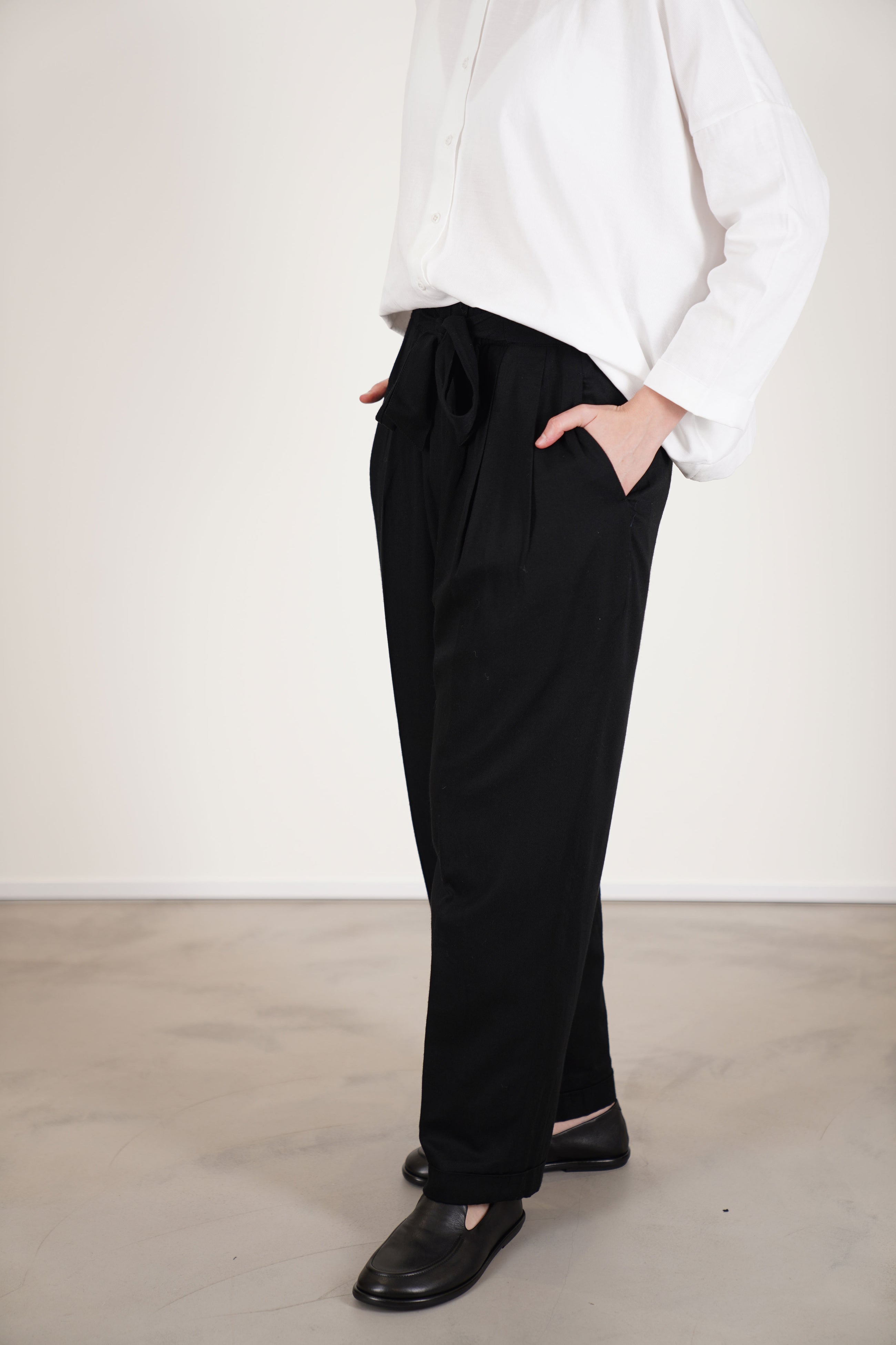 side view of école de curiosités pants patricia black with an elastic waistband with a subtle self-tie, complemented by soft pleats that shape the waist.