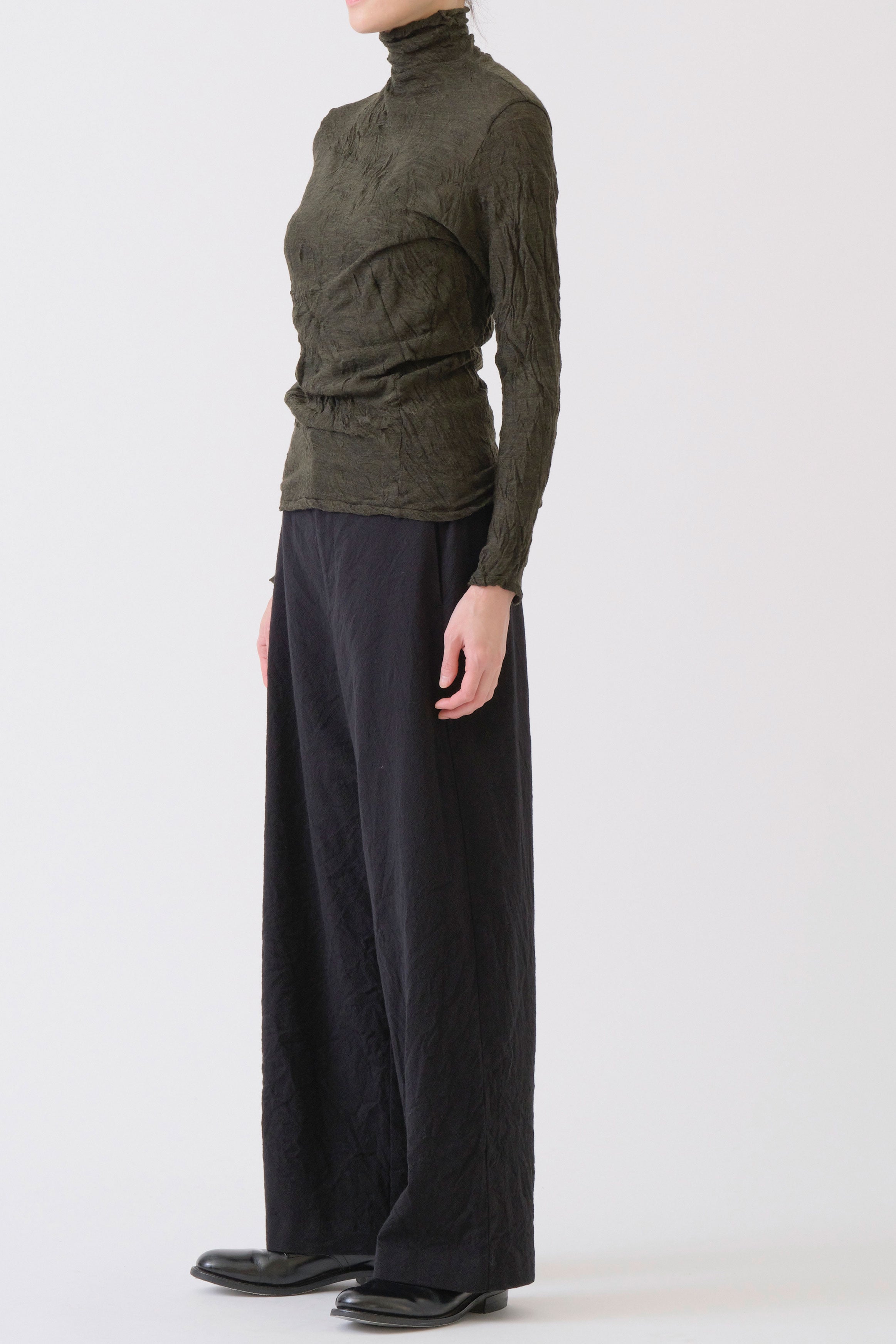 side view of pas de calais wool gauze crinkle turtleneck khaki paired with trousers.