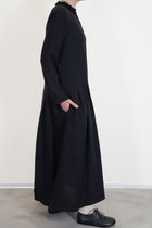 side view of apuntob (a.b) woolen dress black long sleeves with small slit details at the cuffs and a narrow fit on the shoulders. long skirt with pleated details and side pockets, unlined.