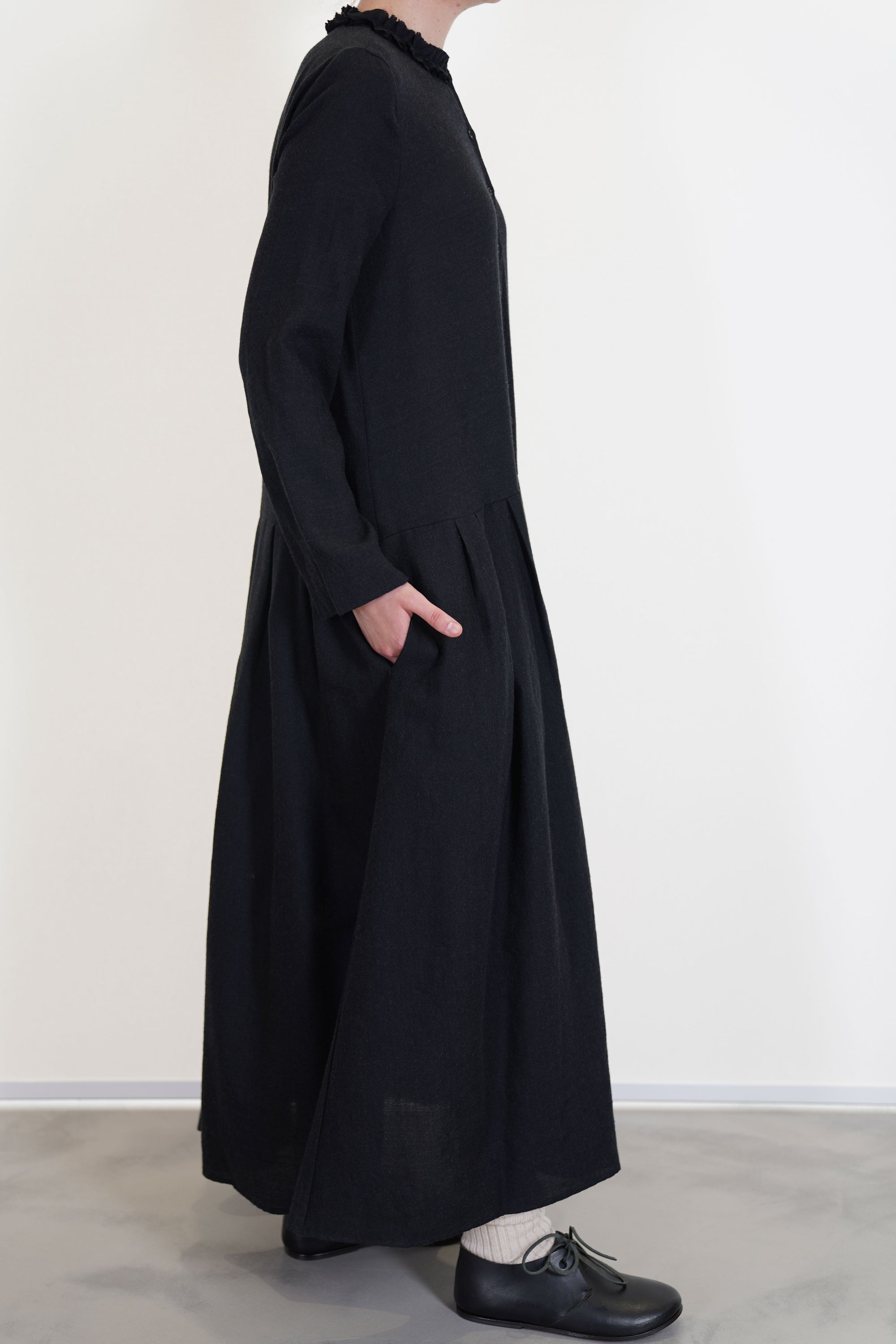 side view of apuntob (a.b) woolen dress black long sleeves with small slit details at the cuffs and a narrow fit on the shoulders. long skirt with pleated details and side pockets, unlined.