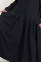detail view of apuntob (a.b) woolen dress black featuring a half panel button front opening and wide pleated details at the skirt