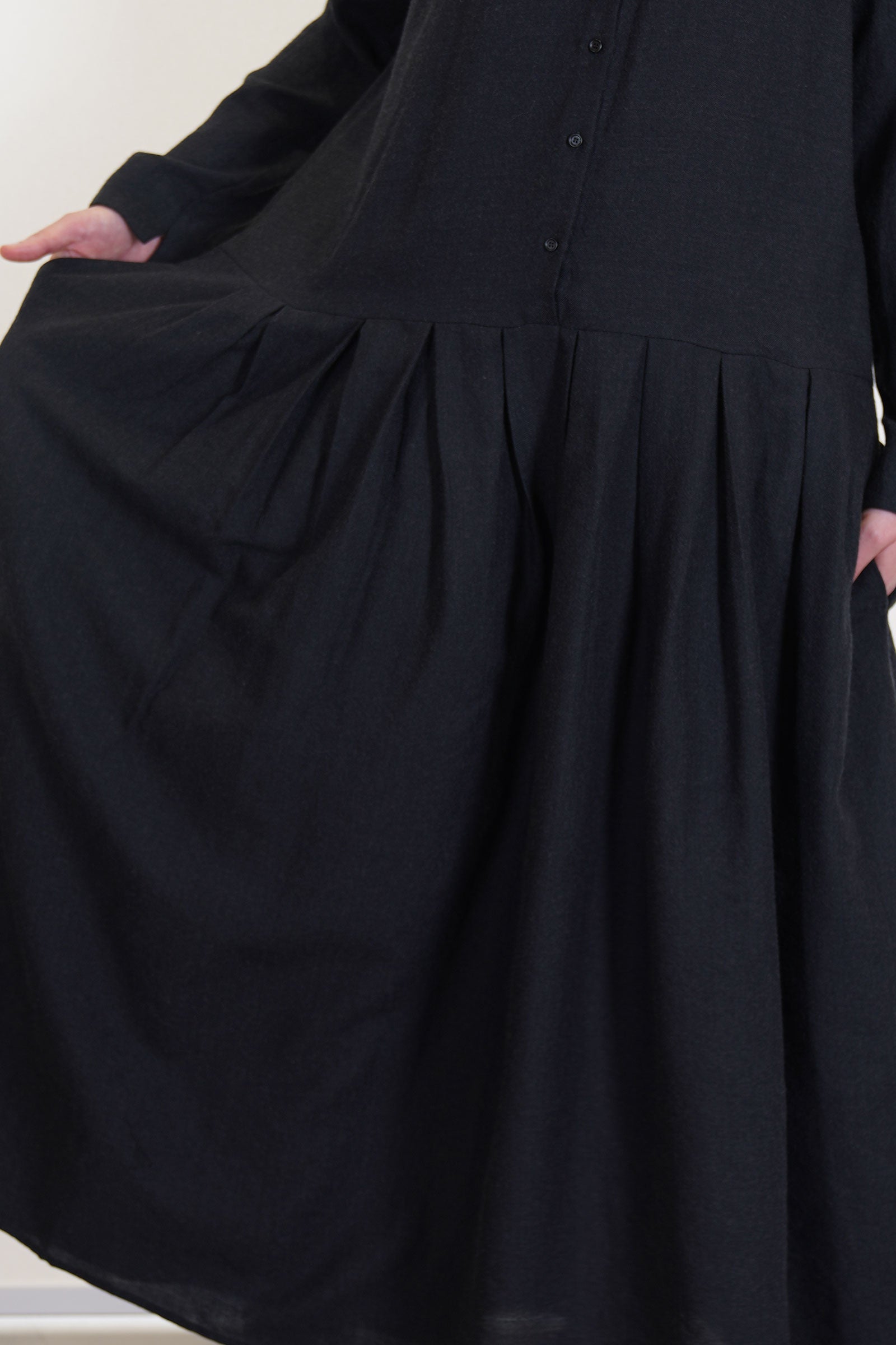 detail view of apuntob (a.b) woolen dress black featuring a half panel button front opening and wide pleated details at the skirt