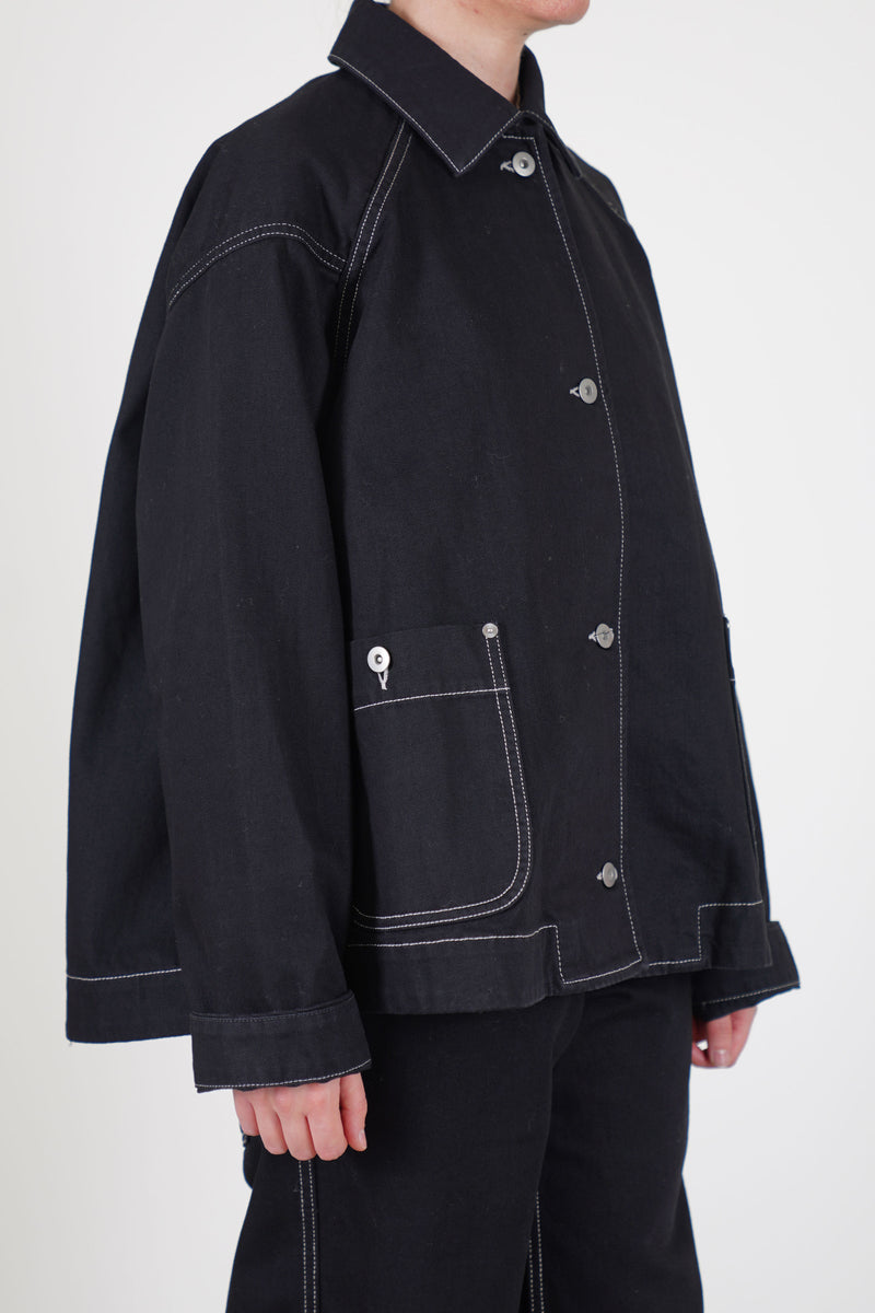 side view of casey casey drays travail jacket denim featuring a button front opening, raglan sleeves and two front patch pockets with button details. 