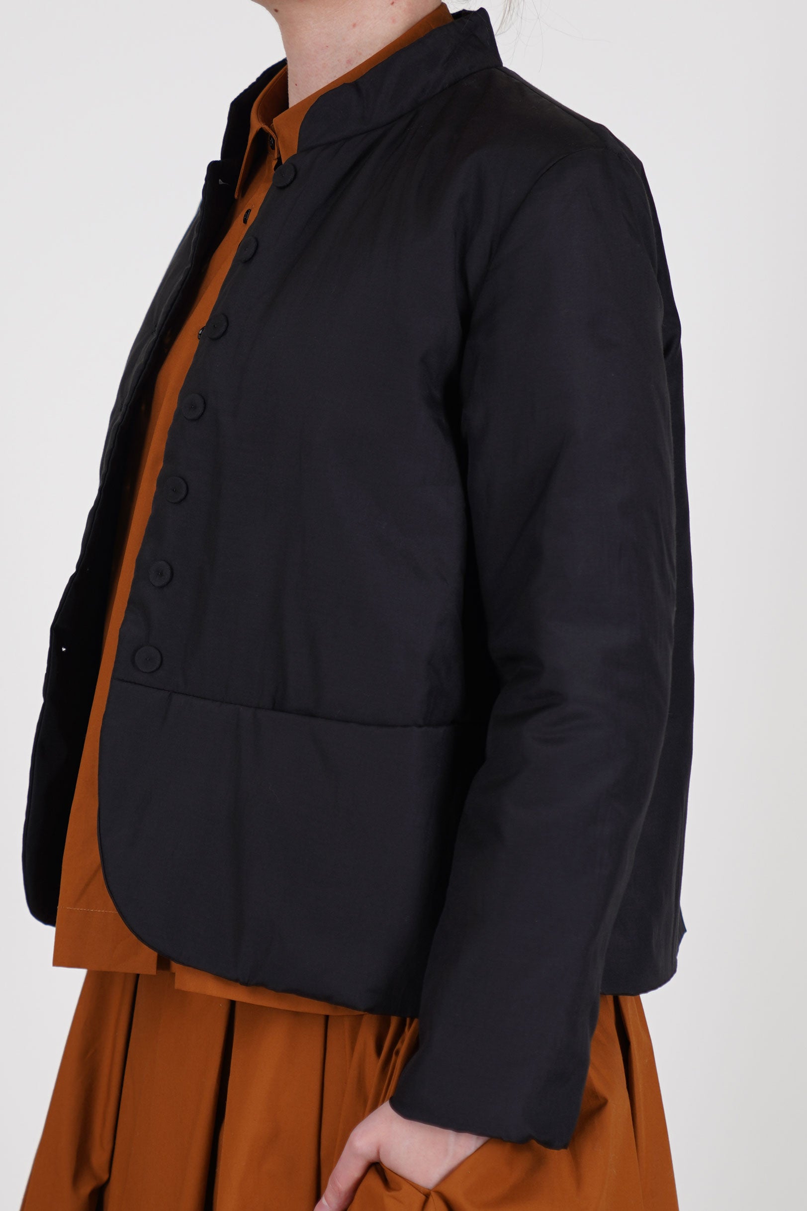 side view of école de curiosités padded jacket jessica silk cotton black finished with fabric-covered buttons down the front and is fully lined in soft cotton for added comfort.