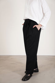 side view of école de curiosités pants patricia black with an elastic waistband with a subtle self-tie, complemented by soft pleats that shape the waist. 
