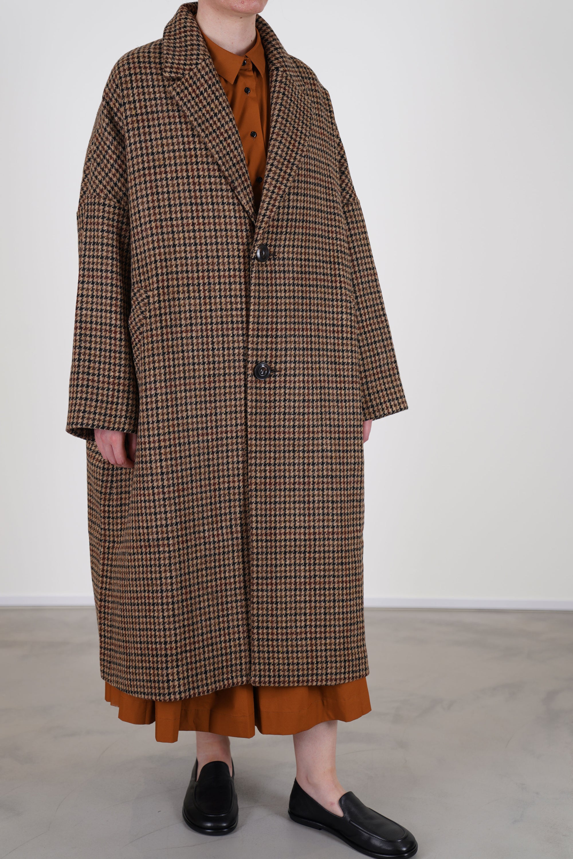 profile view of école de curiosités wool coat coper mix brown relaxed fit, v-neckline and two button front opening